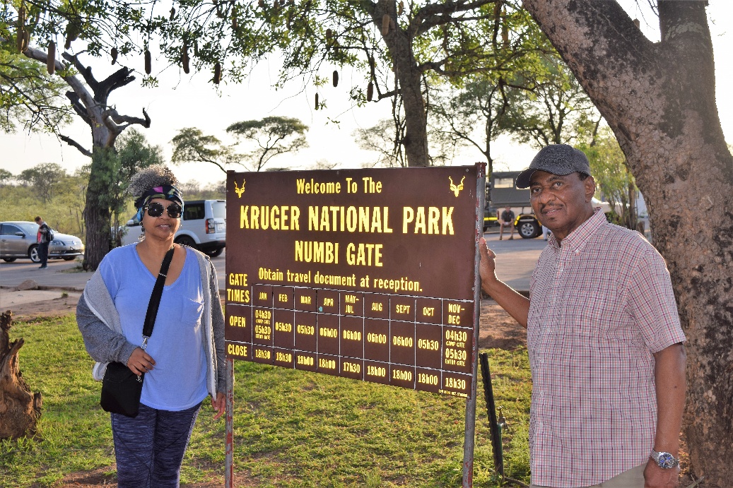 A man and woman stand beside a sign reading Kruger National Park