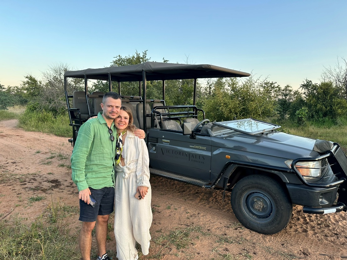 A Man And Woman Stand Beside A Jeep On A Dirt Road