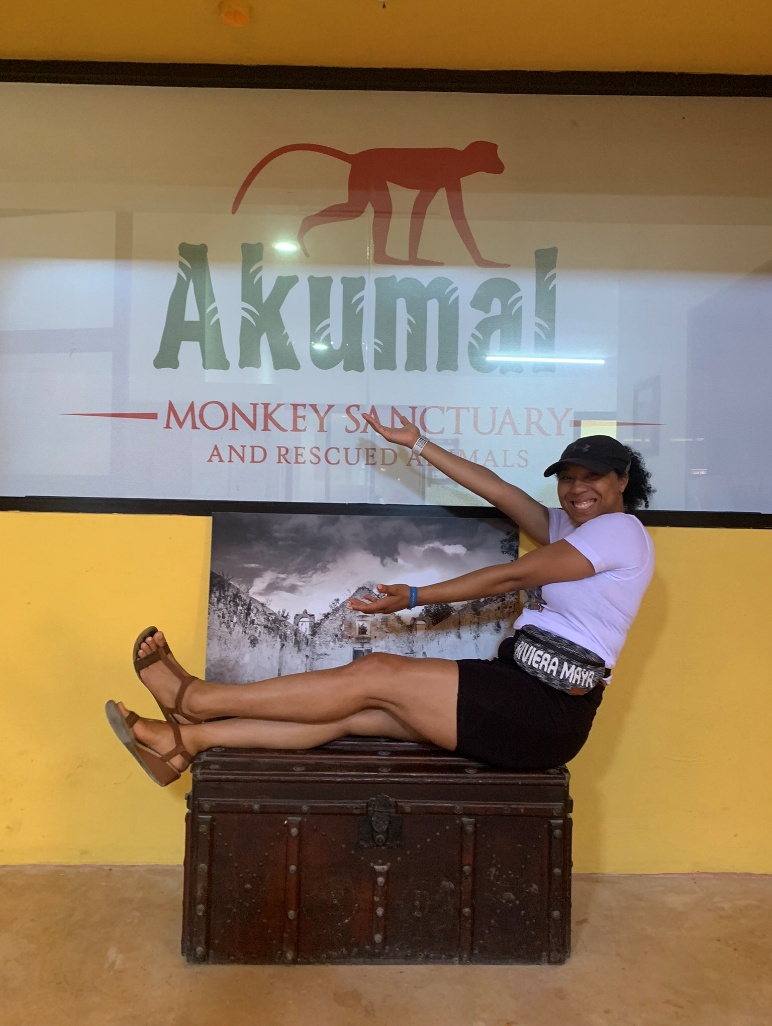 A woman poses cheerfully in front of the "Akumal Monkey Sanctuary" sign